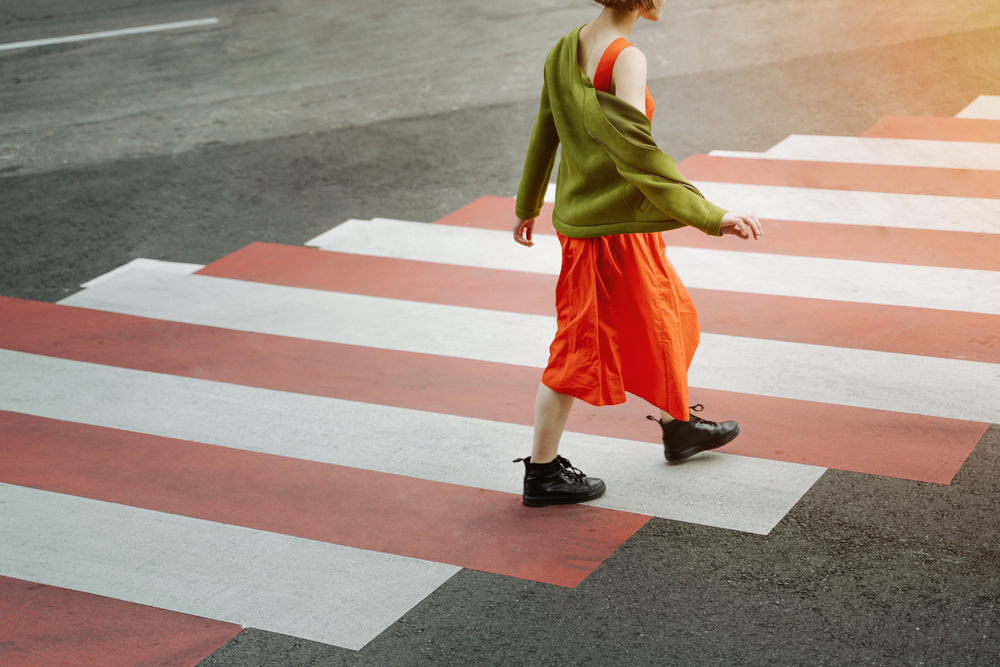 Young girl in red dress and green jacket crosses the road at a pedestrian crossing. metaphor for moving forward, growing up, overcoming difficulties and problems. Stylish fashion catwalk in big city